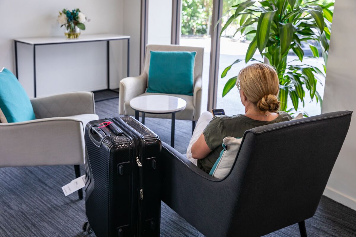 A hotel room with a seating area featuring a sofa and a chair, a small round table, and a black suitcase on the floor.