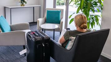 A hotel room with a seating area featuring a sofa and a chair, a small round table, and a black suitcase on the floor.