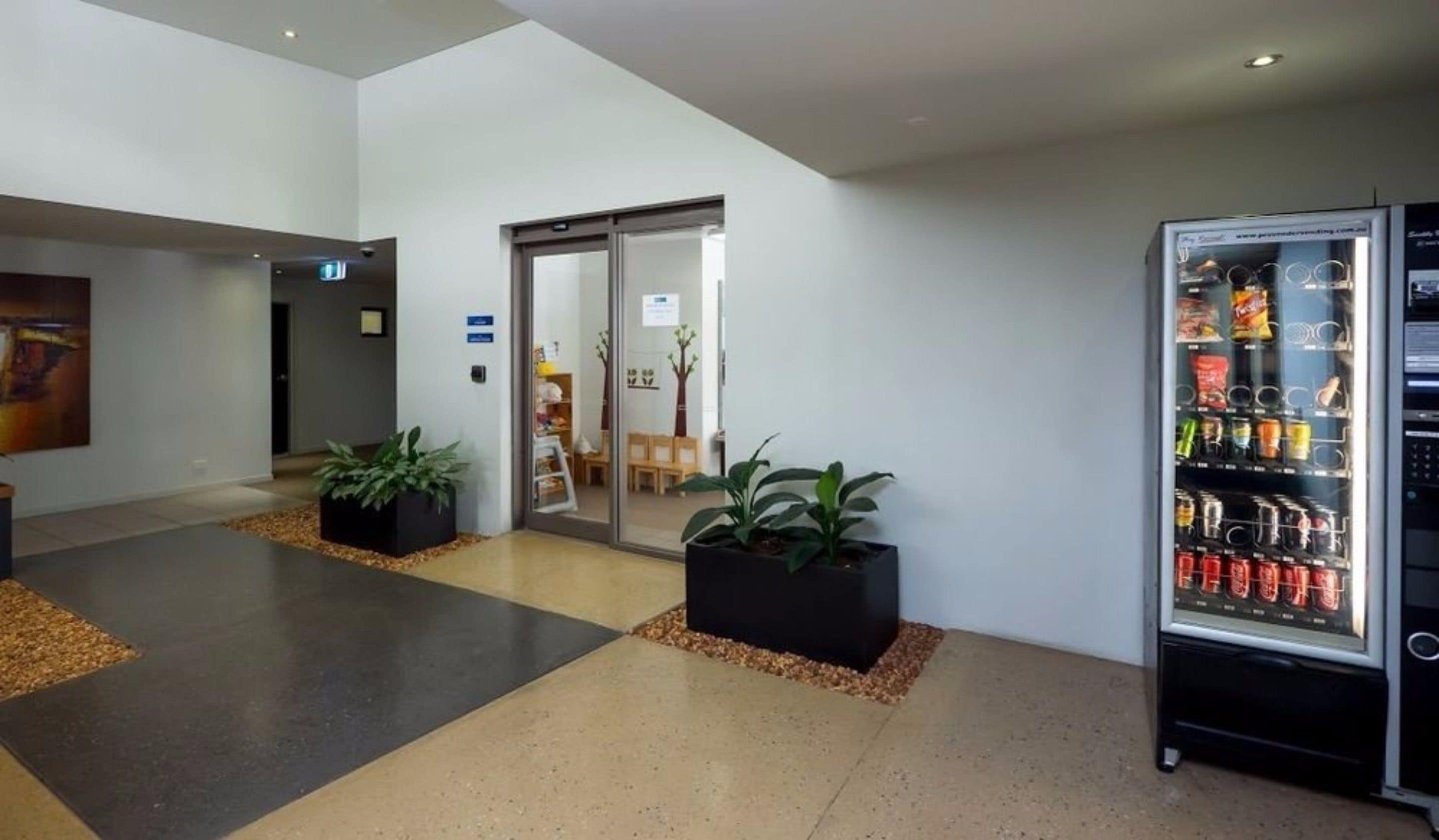 A modern lobby with a vending machine, potted plants, and a seating area.