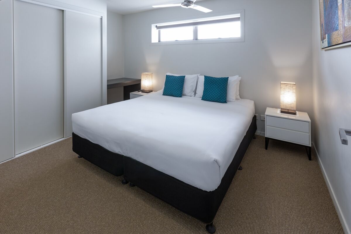 A modern hotel room with a large bed, two bedside tables with lamps, a ceiling fan, and a window providing natural light.