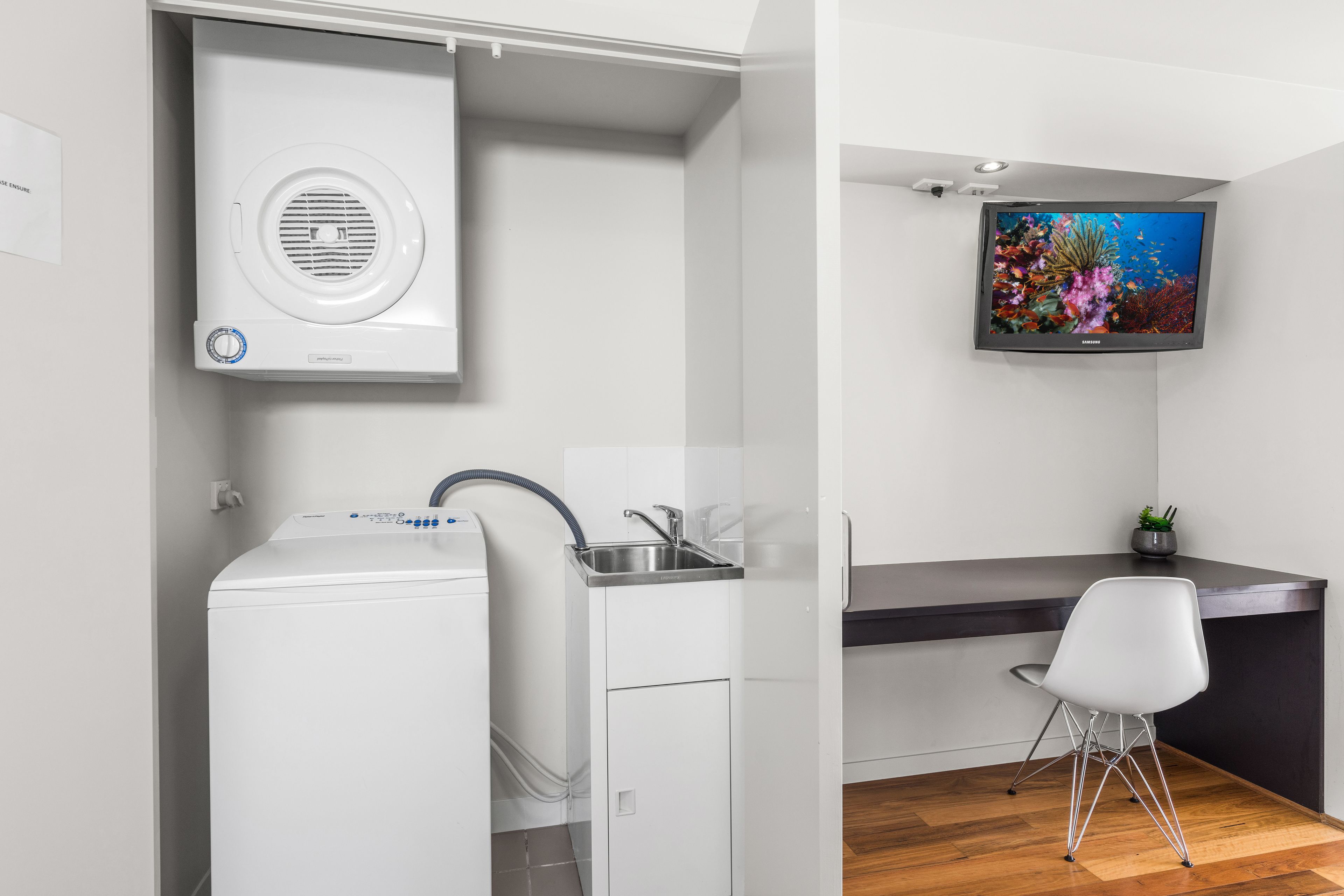 Een praktische keuken met een ingebouwde wasmachine, een spoelbak en een flatscreen televisie aan de muur.