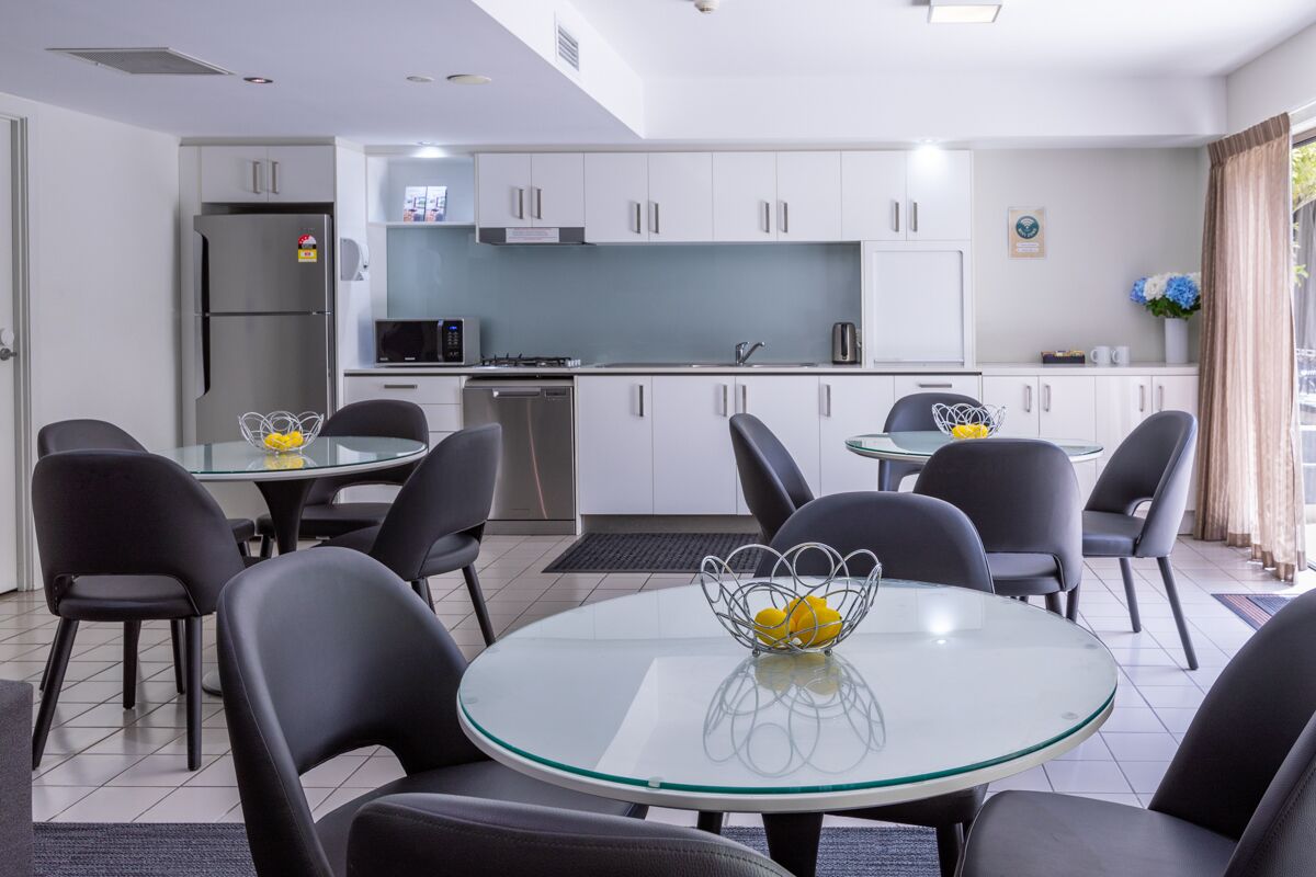 A modern kitchen with white cabinets, a stainless steel refrigerator, and a dining area with black chairs and a glass table.
