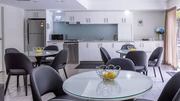 A modern kitchen with white cabinets, a stainless steel refrigerator, and a dining area with black chairs and a glass table.