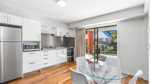 A modern kitchen with white cabinets, stainless steel appliances, and a glass dining table with white chairs. - Essence Apartments Chermside (Chermside)