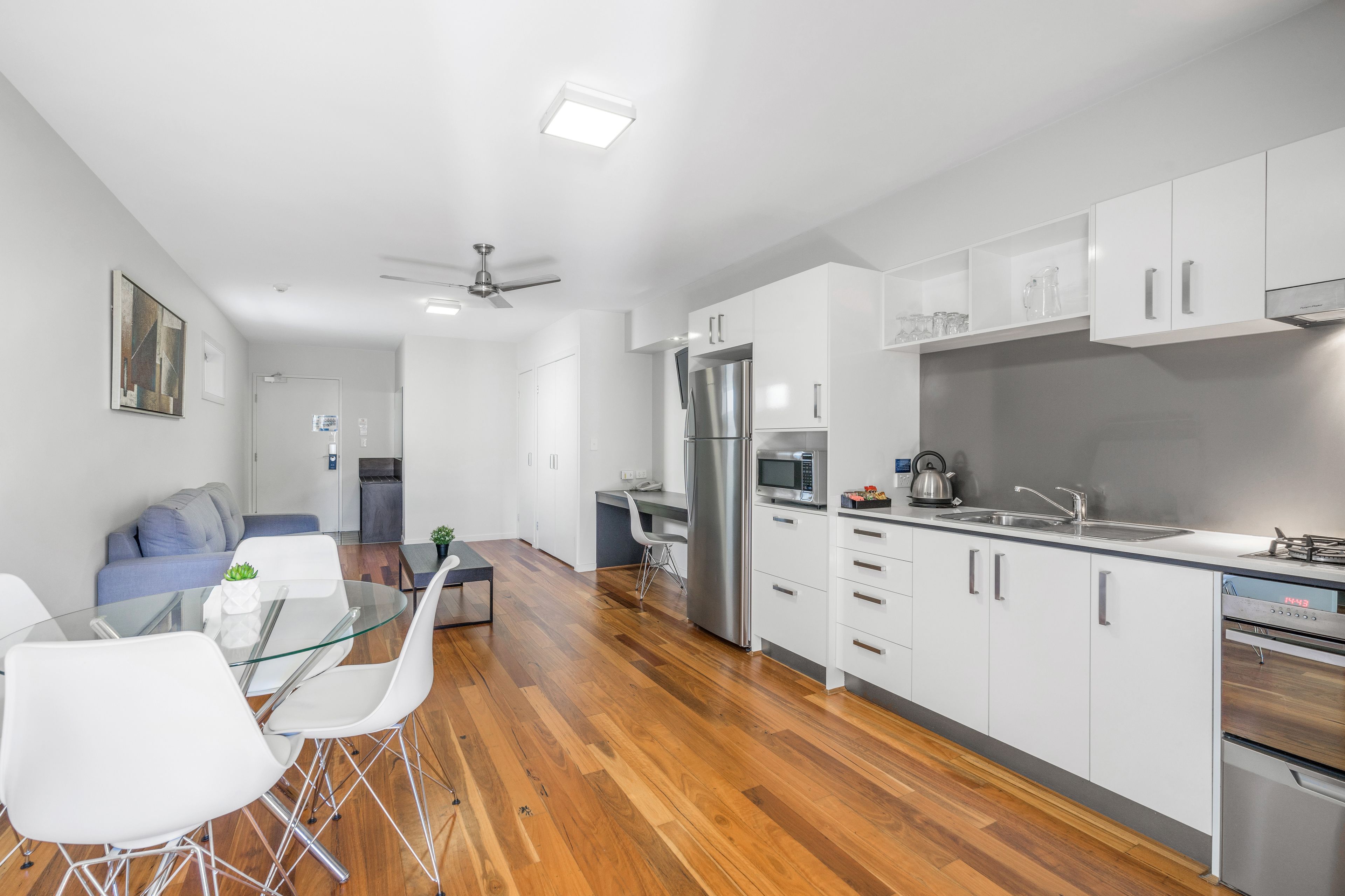 Una cocina moderna con armarios blancos, electrodomésticos de acero inoxidable y una mesa de comedor de vidrio.