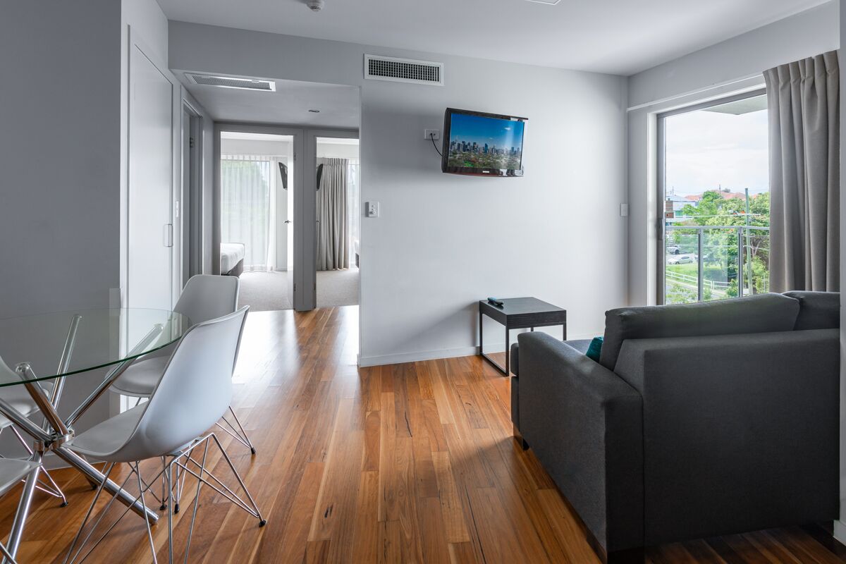 Una sala de estar moderna con un sofá, una mesa de comedor de vidrio con sillas, un televisor de pantalla plana montado en la pared y un ventanal con cortinas.