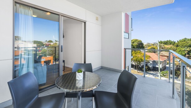 A balcony with a round table and chairs, a potted plant, and a view of the cityscape. - Essence Apartments Chermside (Chermside)