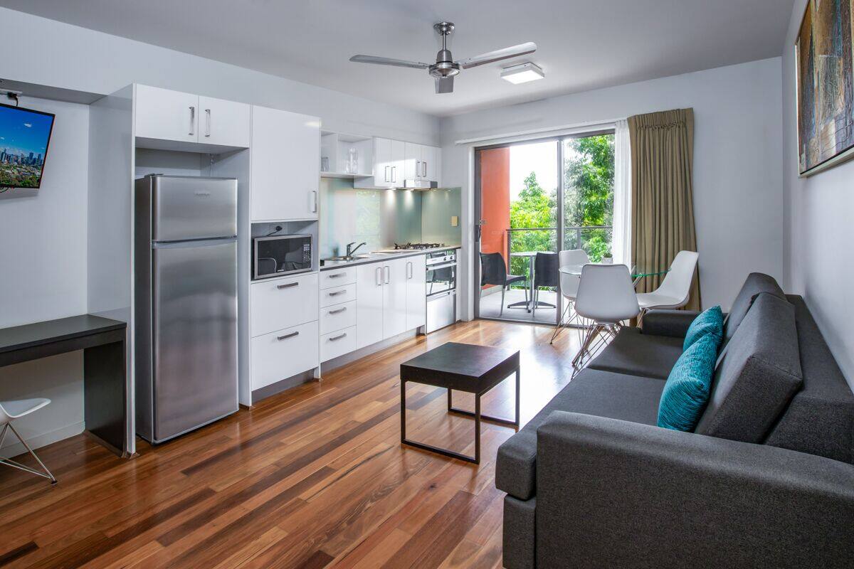 A modern kitchen with white cabinets, a stainless steel refrigerator, and a dining area with a gray sofa and teal pillow.