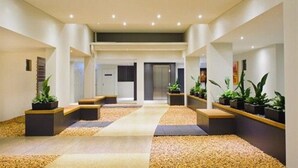 A modern hotel lobby with a central seating area, potted plants, and a tiled floor. - Essence Apartments Chermside (Chermside)