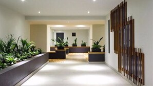 A modern hallway with a central seating area, potted plants, and a decorative wooden panel on the right. - Essence Apartments Chermside (Chermside)
