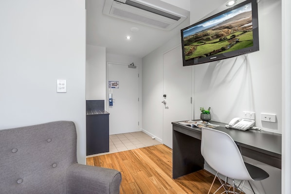 Un espacio de oficina moderno con un escritorio, una silla y un televisor montado que muestra un paisaje pintoresco.