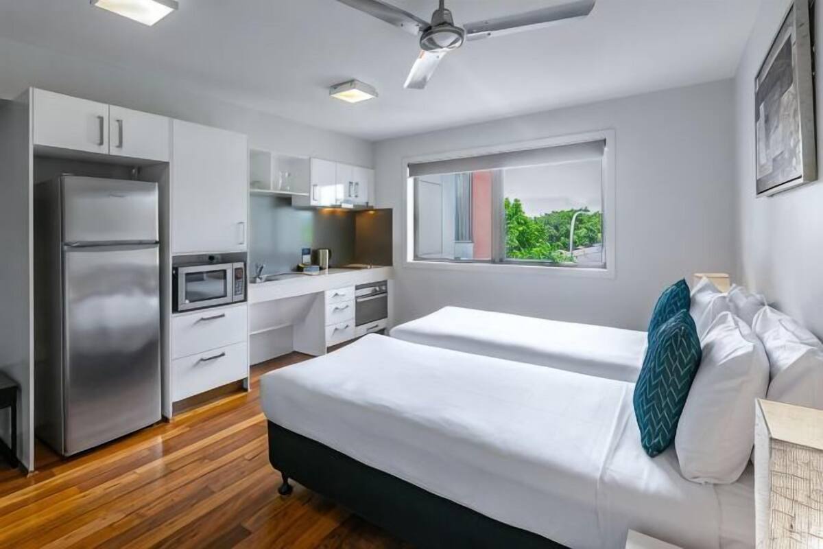 A modern bedroom with a bed, a window, and a kitchenette.