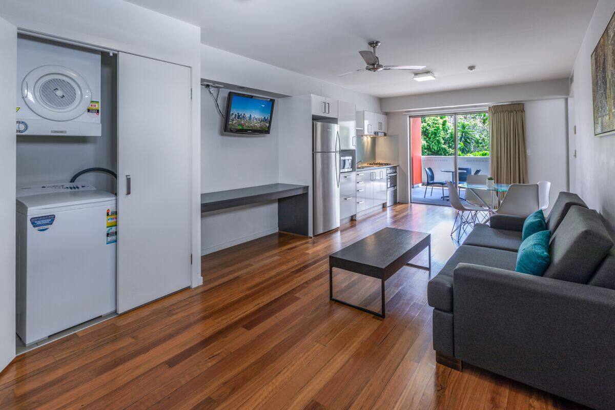 A modern kitchen with built-in appliances, a dining area with a sofa, and a view of greenery outside.