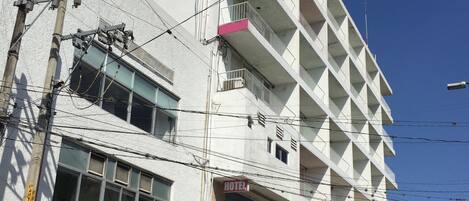 Egy feltűnő „HOTEL” felirattal ellátott szállodai épület, számos eréllyel, és a földszinten található bejárattal, melyhez egy parkoló is tartozik.