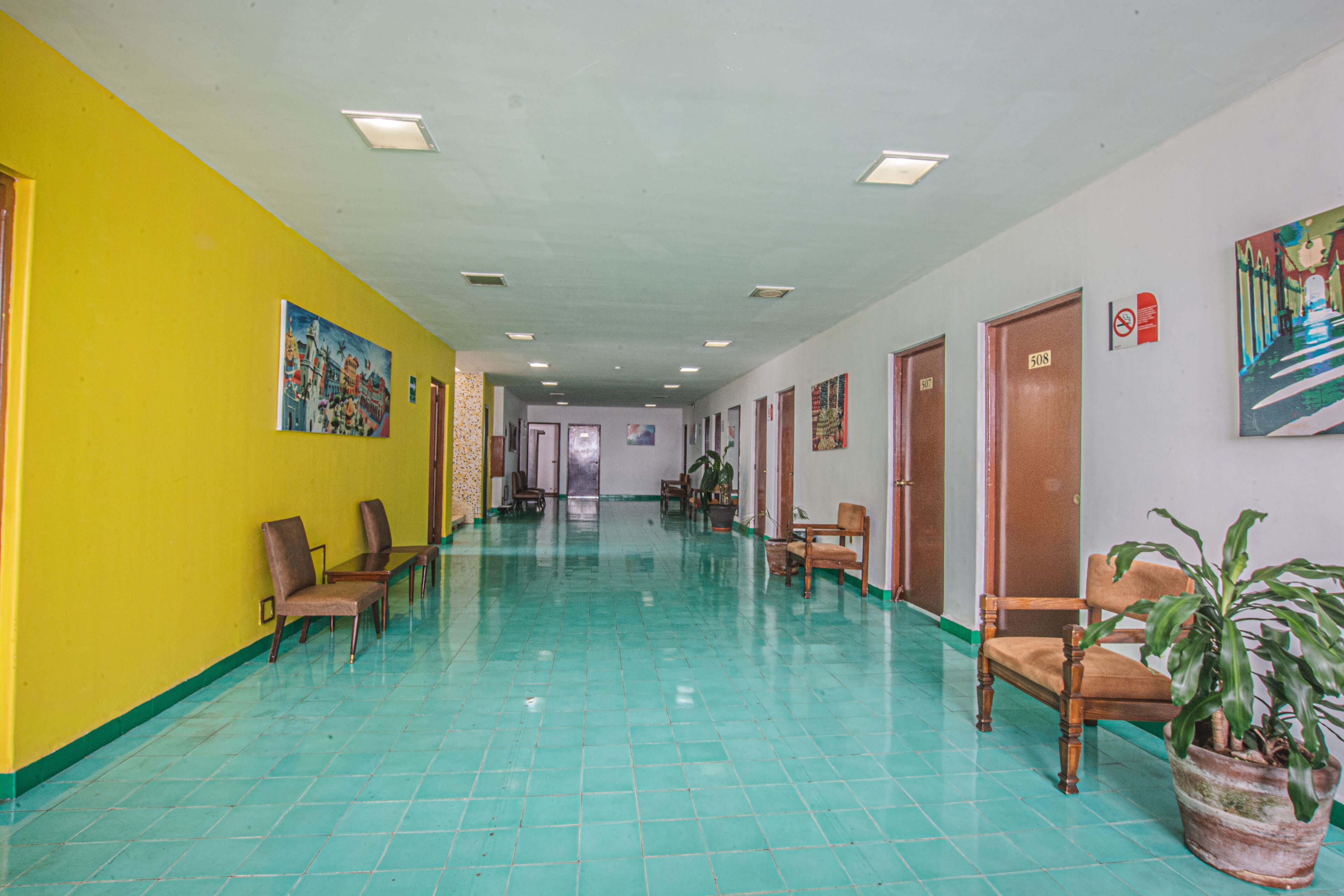 A hallway with teal-tiled floors, wooden chairs, and a potted plant.