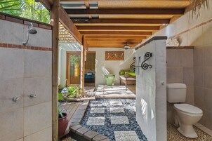 A bathroom with a tiled floor, a shower, a toilet, and a decorative wall piece.