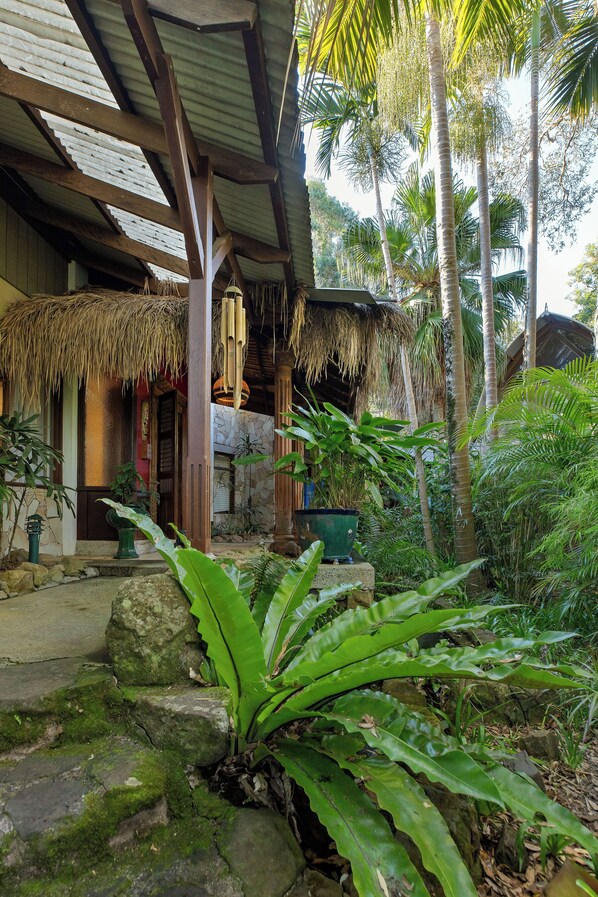 Um jardim tropical com uma estrutura de telhado de palha, plantas verdes exuberantes e palmeiras.