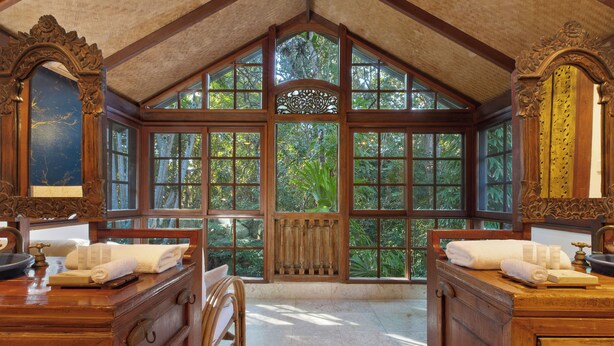 A room with large windows, wooden furniture, and a view of greenery outside. - The Garden Burees (Byron Bay)