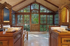 A room with large windows, wooden furniture, and a view of greenery outside. - The Garden Burees (Byron Bay)