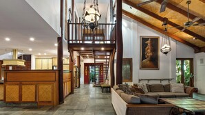 A spacious interior with a high ceiling, a central staircase, a reception area, and a seating area with a sofa and coffee table. - The Garden Burees (Byron Bay)