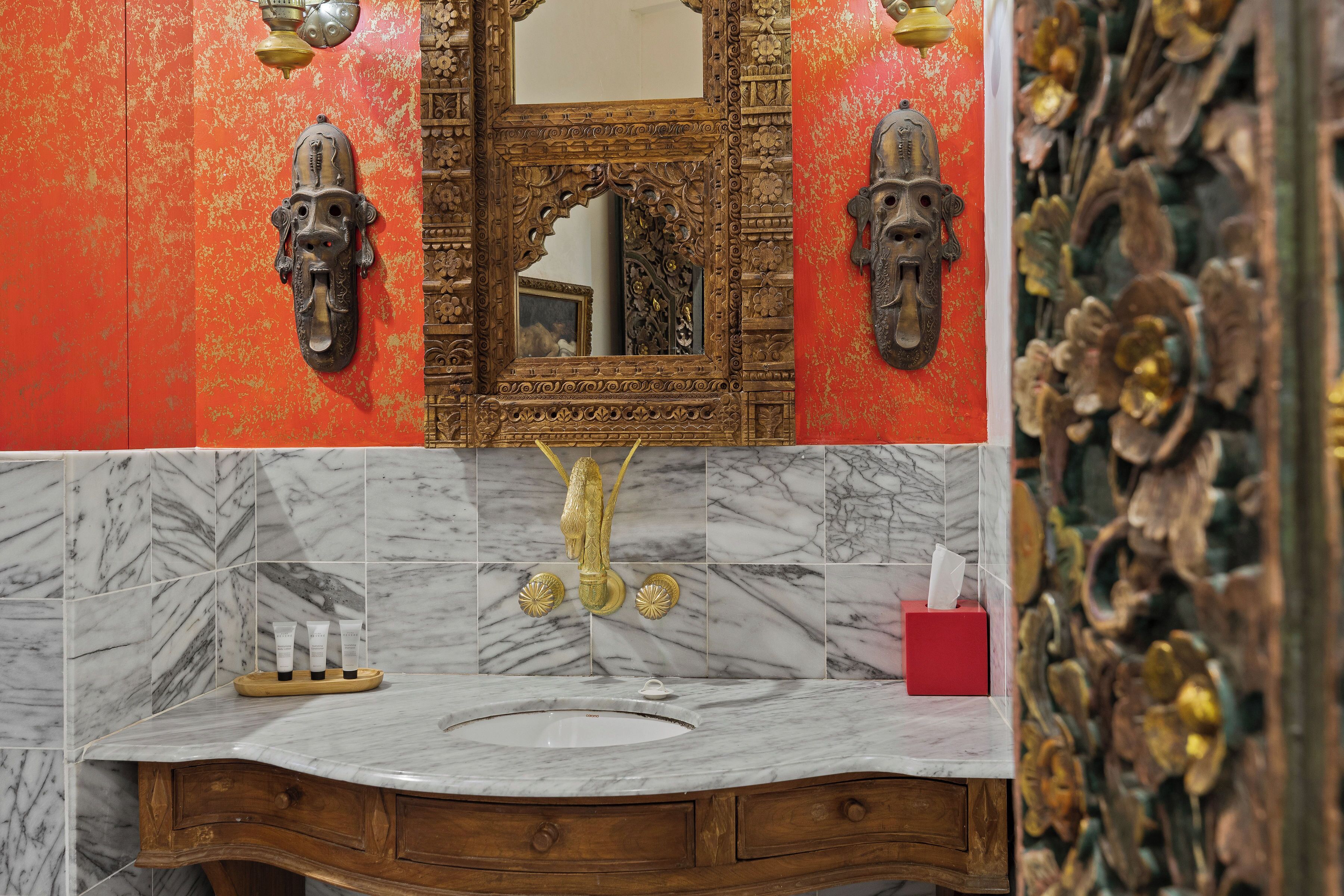 A bathroom with ornate wall decor, a marble sink, and a wooden vanity.