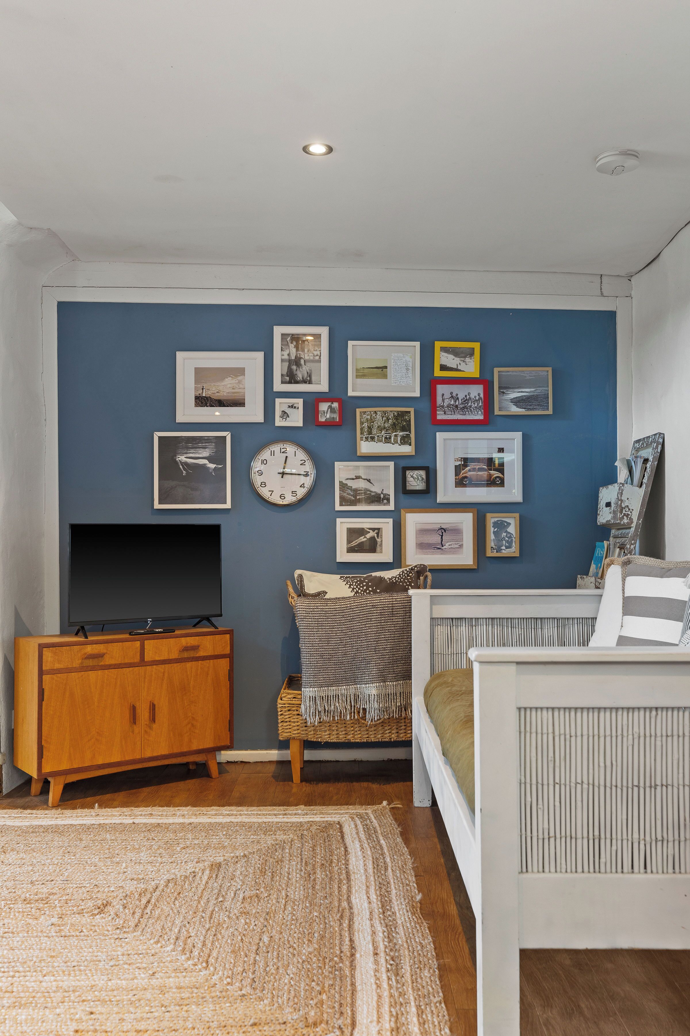 A room with a blue wall, wooden furniture, a flat-screen TV, and various framed pictures.