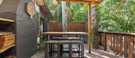 An outdoor patio with a wooden table and benches, surrounded by a wooden fence and lush greenery.