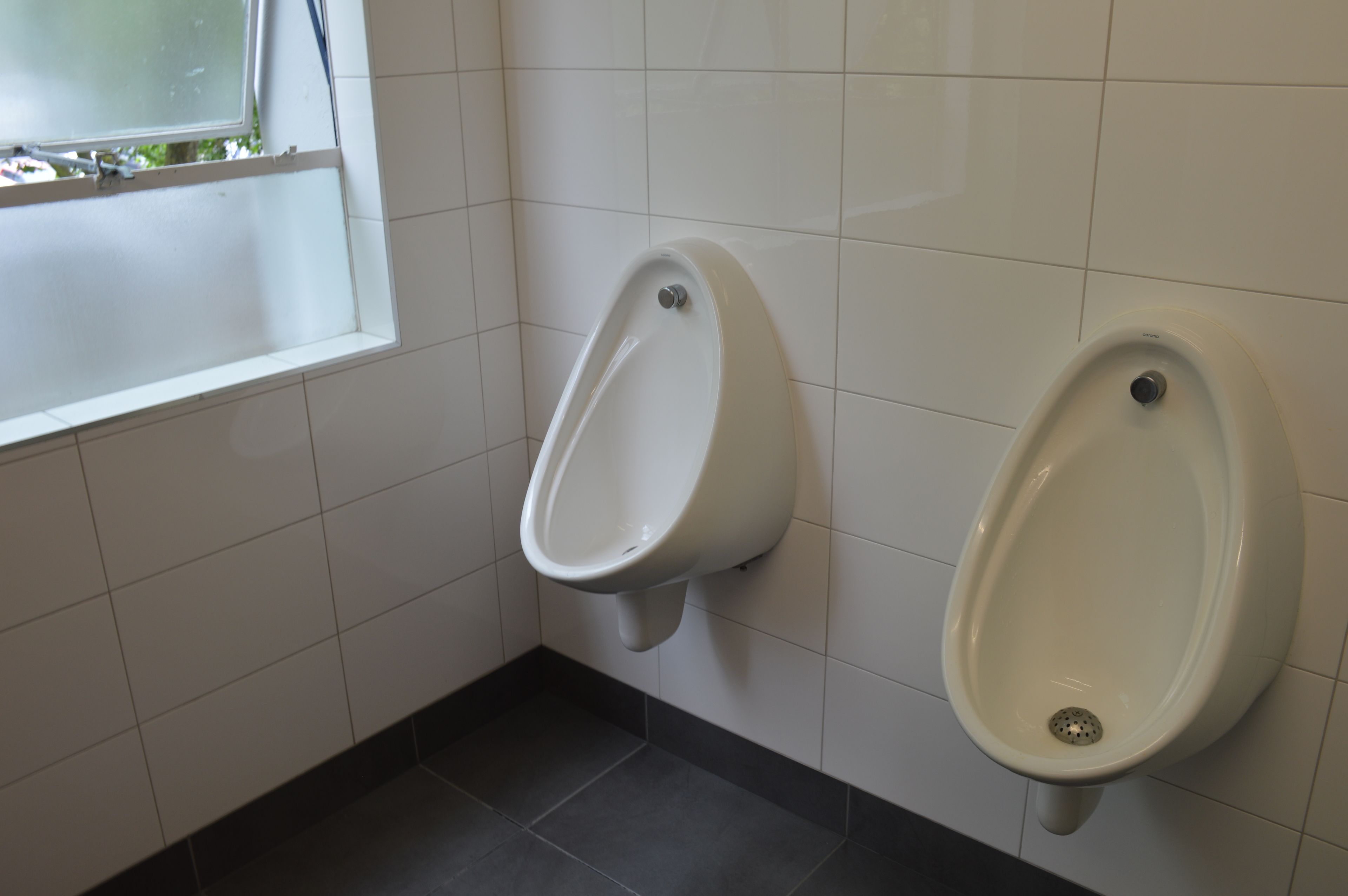 A restroom with two urinals mounted on a tiled wall.