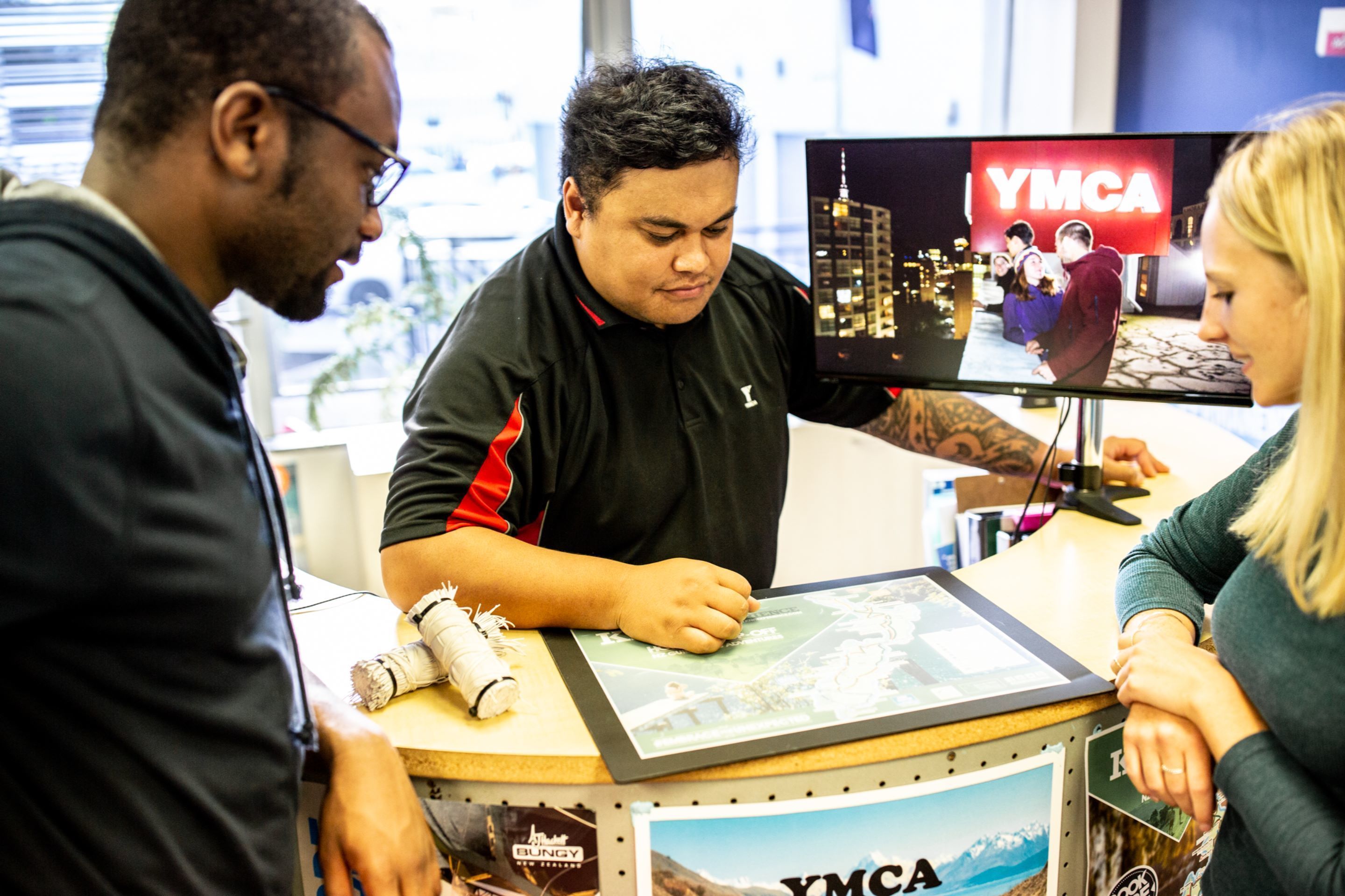 A reception desk with a monitor displaying 'YMCA' and a framed map.