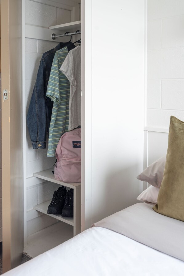 A bedroom with a bed, a closet with hanging clothes and shoes, and a pillow on the bed.