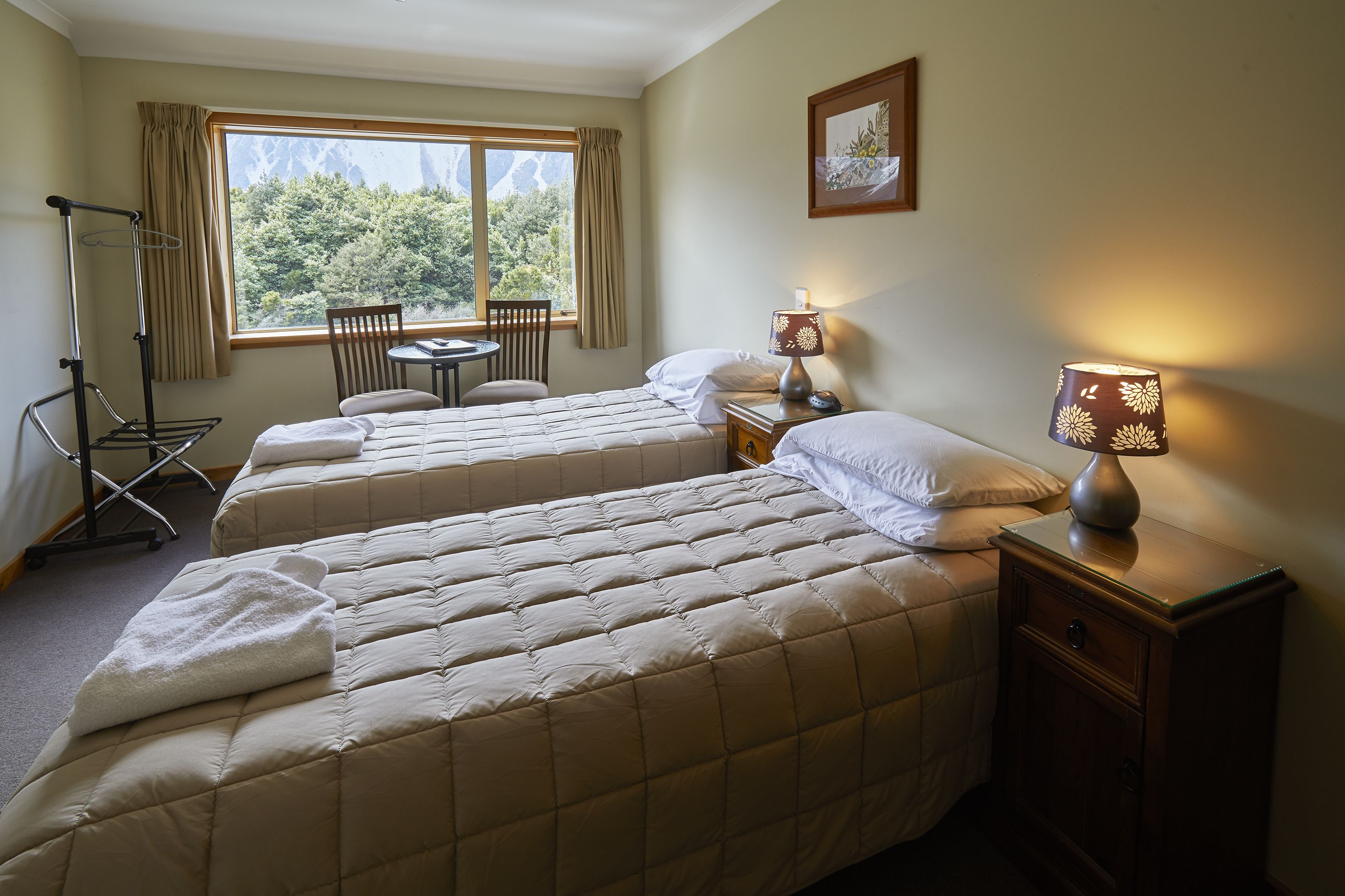 A hotel room with two beds, a desk, a chair, and a window with a view of mountains.