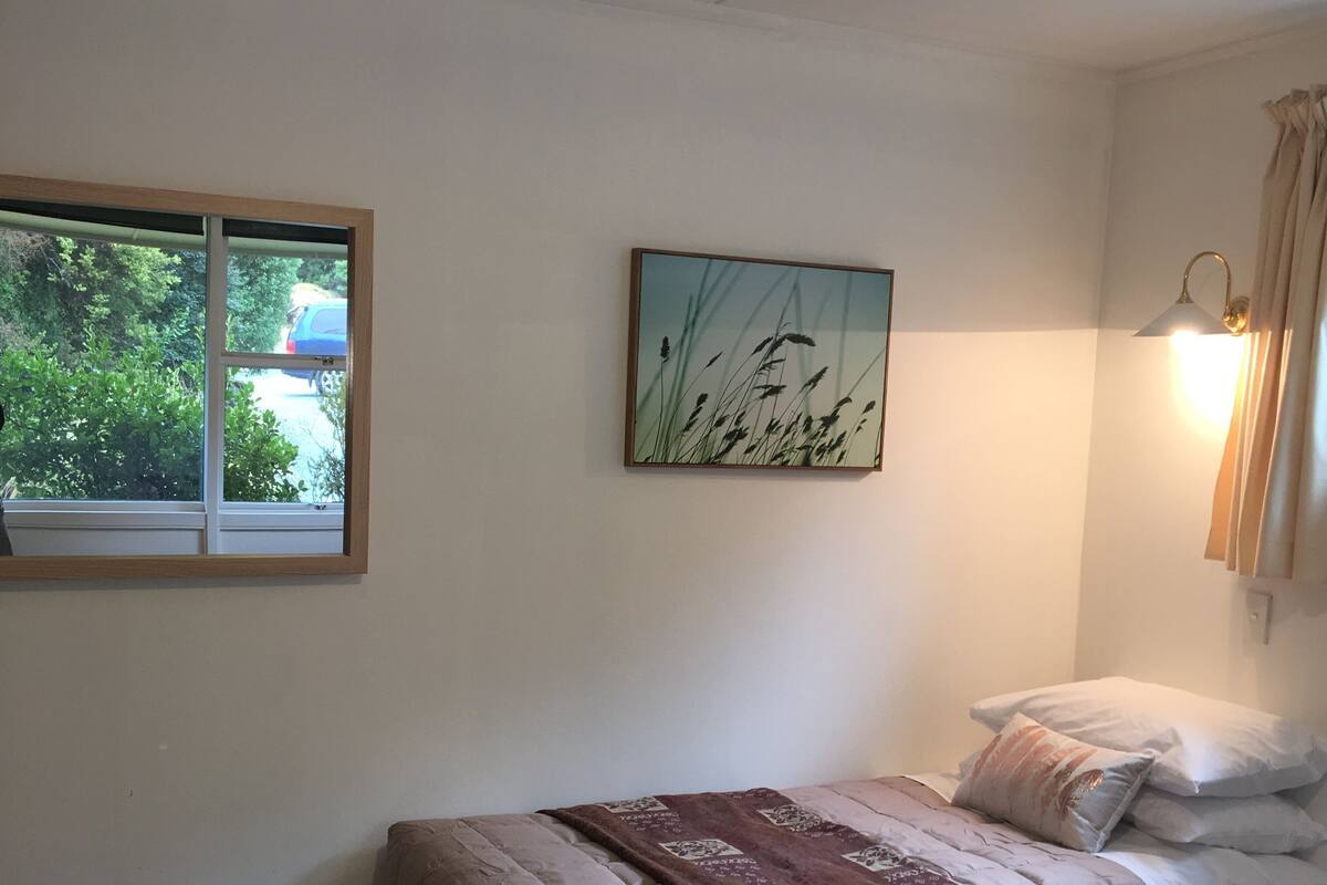 Un dormitorio con una cama, una ventana, un cuadro colgado en la pared y una lámpara de pared.