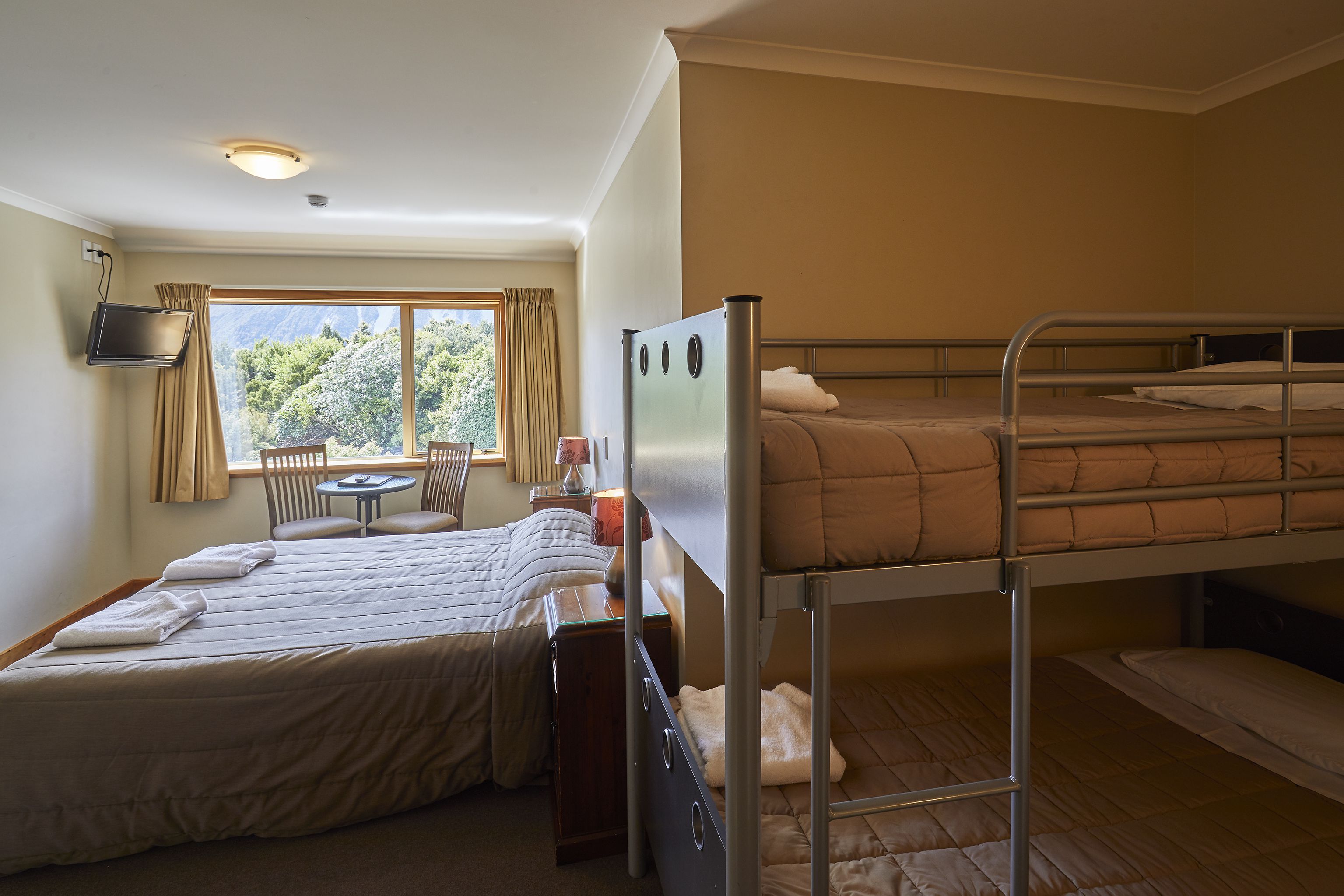 A room with two beds, a small table, and a window with curtains.