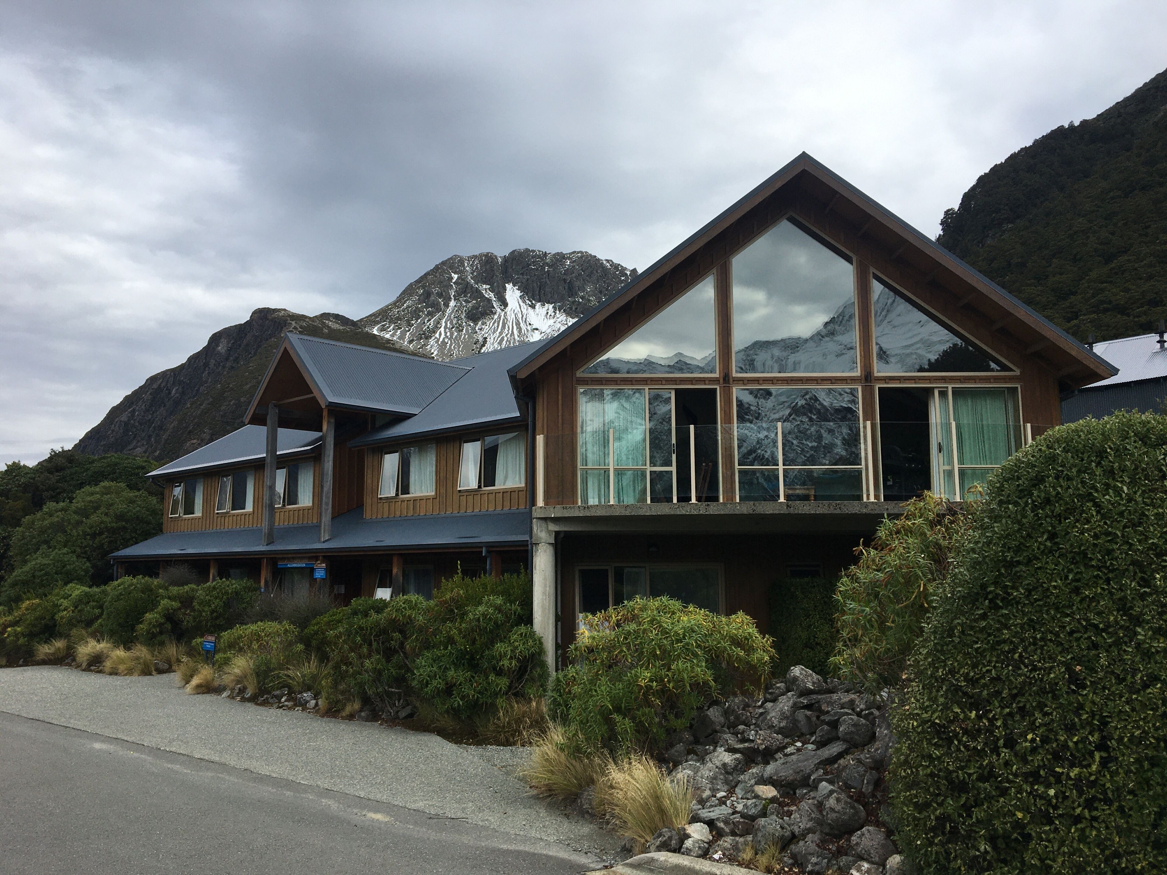 A two-story wooden building with large windows and a mountain backdrop.