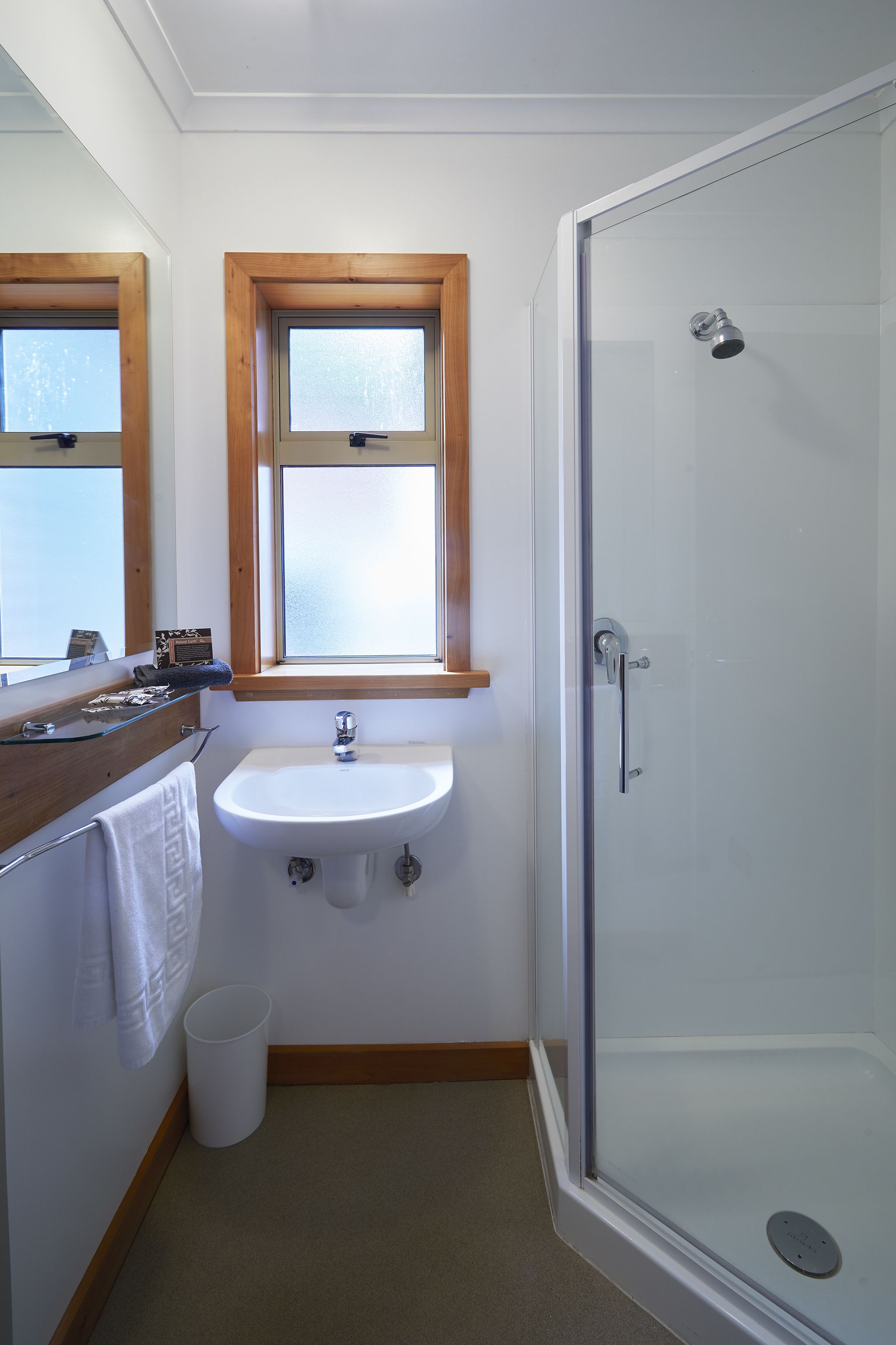 Ein Badezimmer mit Duschkabine aus Glas, einem weißen Waschbecken und einem Fenster über dem Waschbecken.