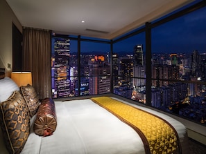 Habitación de hotel con una cama grande, vista nocturna de la ciudad y una ventana con cortinas.