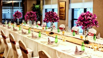 Una larga mesa de banquete vestida con manteles blancos, botellas verdes y flores púrpuras.