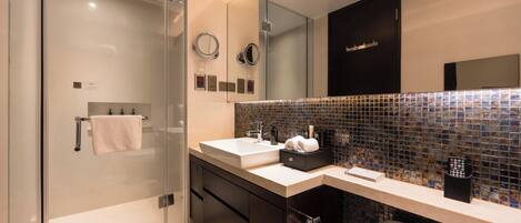 A modern bathroom with a glass shower enclosure, a white sink, a black cabinet, and a tiled backsplash.
