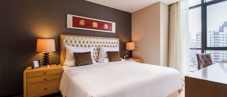 A modern hotel room with a large bed, bedside tables with lamps, a desk, and a view of the city through large windows.