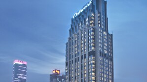 Een hoog gebouw met verlichte reclameborden, met een modern architectonisch ontwerp, veel ramen en een opvallend bord bovenop.