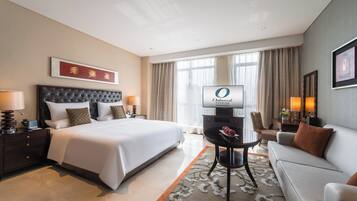 A hotel room with a large bed, a flat-screen TV, a sofa, and a dining table.