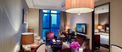 Une chambre d’hôtel comprenant un coin repas, un canapé, une télévision et une vue sur la ville.