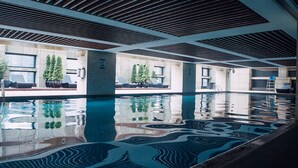 Een groot binnenzwembad met een modern design, voorzien van een geometrisch patroon op de vloer en een plafond met horizontale lamellen.