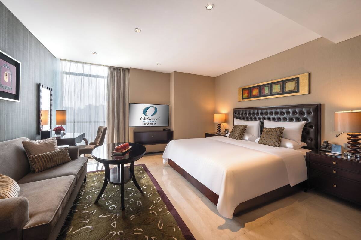 A hotel room with a large bed, a sofa, a dining table, and a TV.