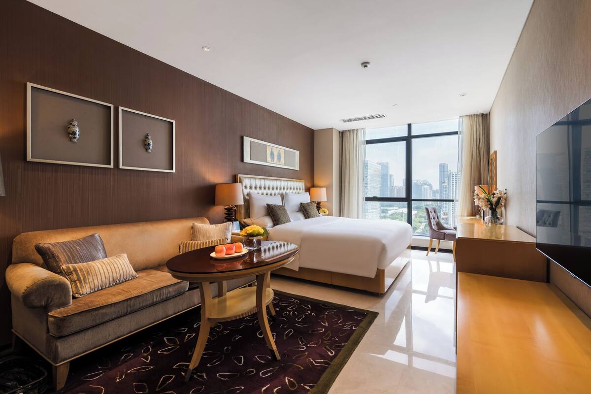 A modern hotel room with a bed, a sofa, a dining table, and a TV.
