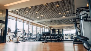 Een ruime sportschool met diverse fitnessapparaten, grote ramen en een modern plafondontwerp.
