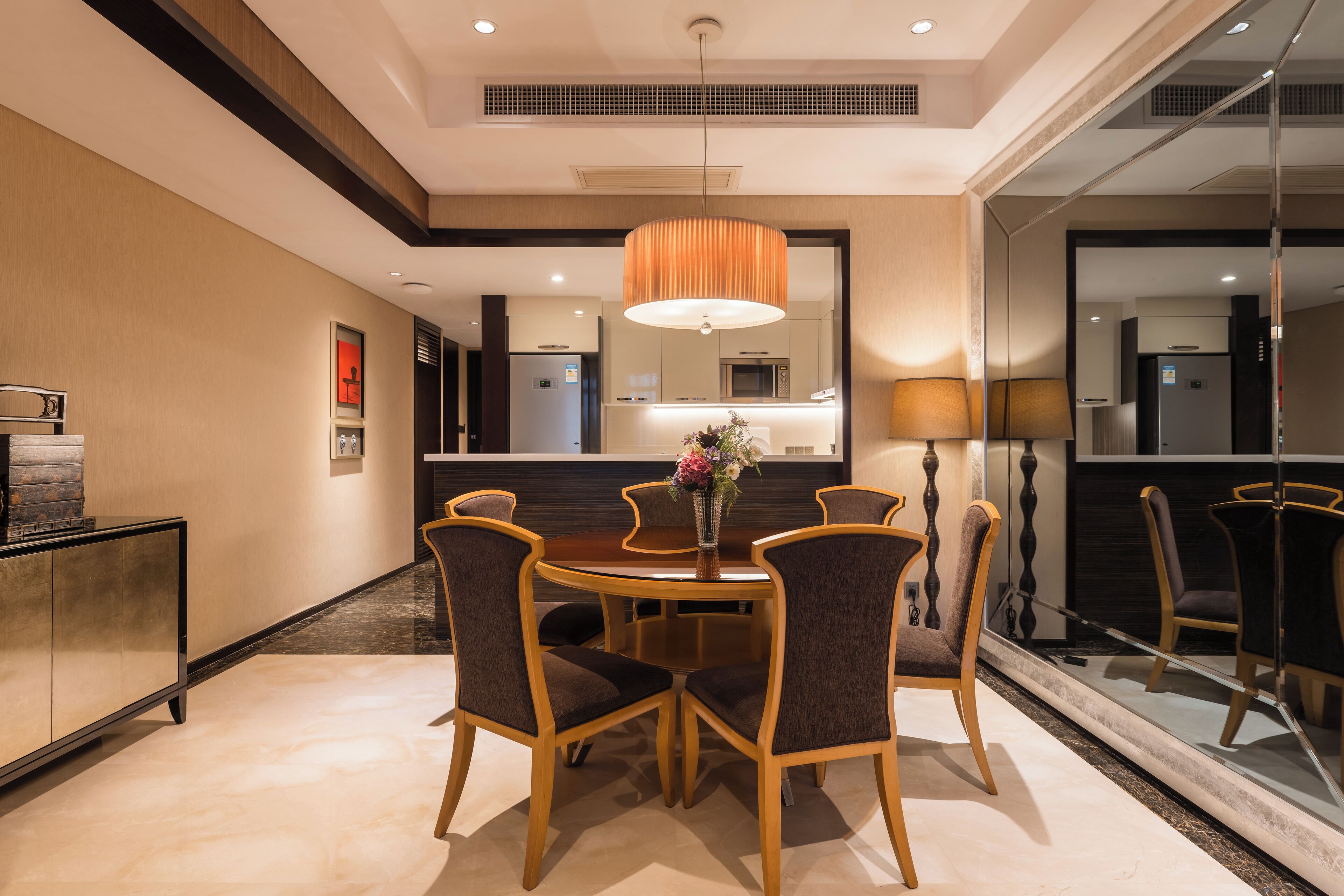 A dining area with a round table, six chairs, a vase with flowers, and a pendant light.