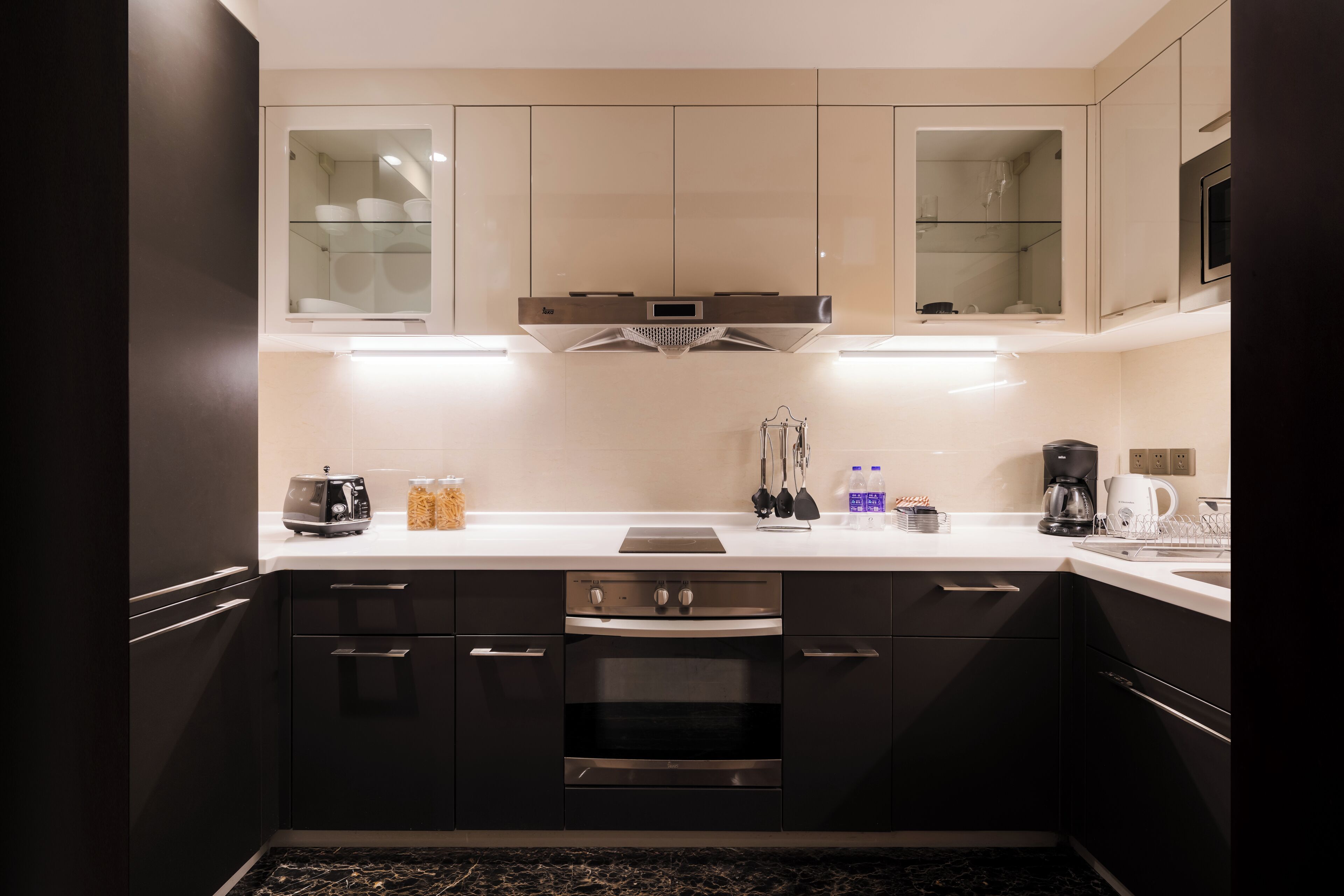 A modern kitchen with dark cabinets, a stainless steel range hood, and a white countertop.
