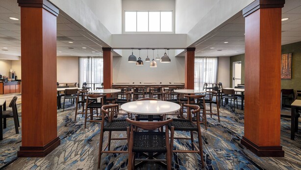 A spacious hotel lobby with multiple round tables and chairs, wooden pillars, and hanging pendant lights. - Fairfield Inn & Suites Visalia Tulare (Tulare)