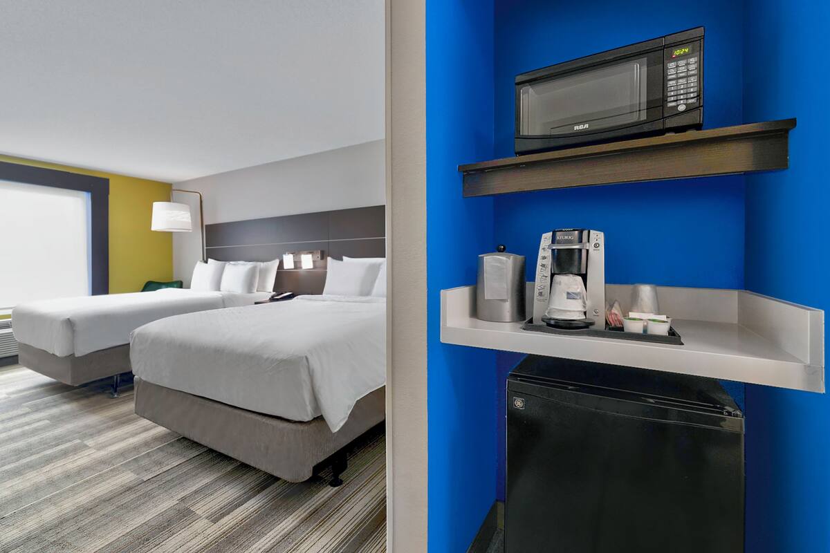 Habitación de hotel con dos camas, microondas, cafetera y refrigerador pequeño.